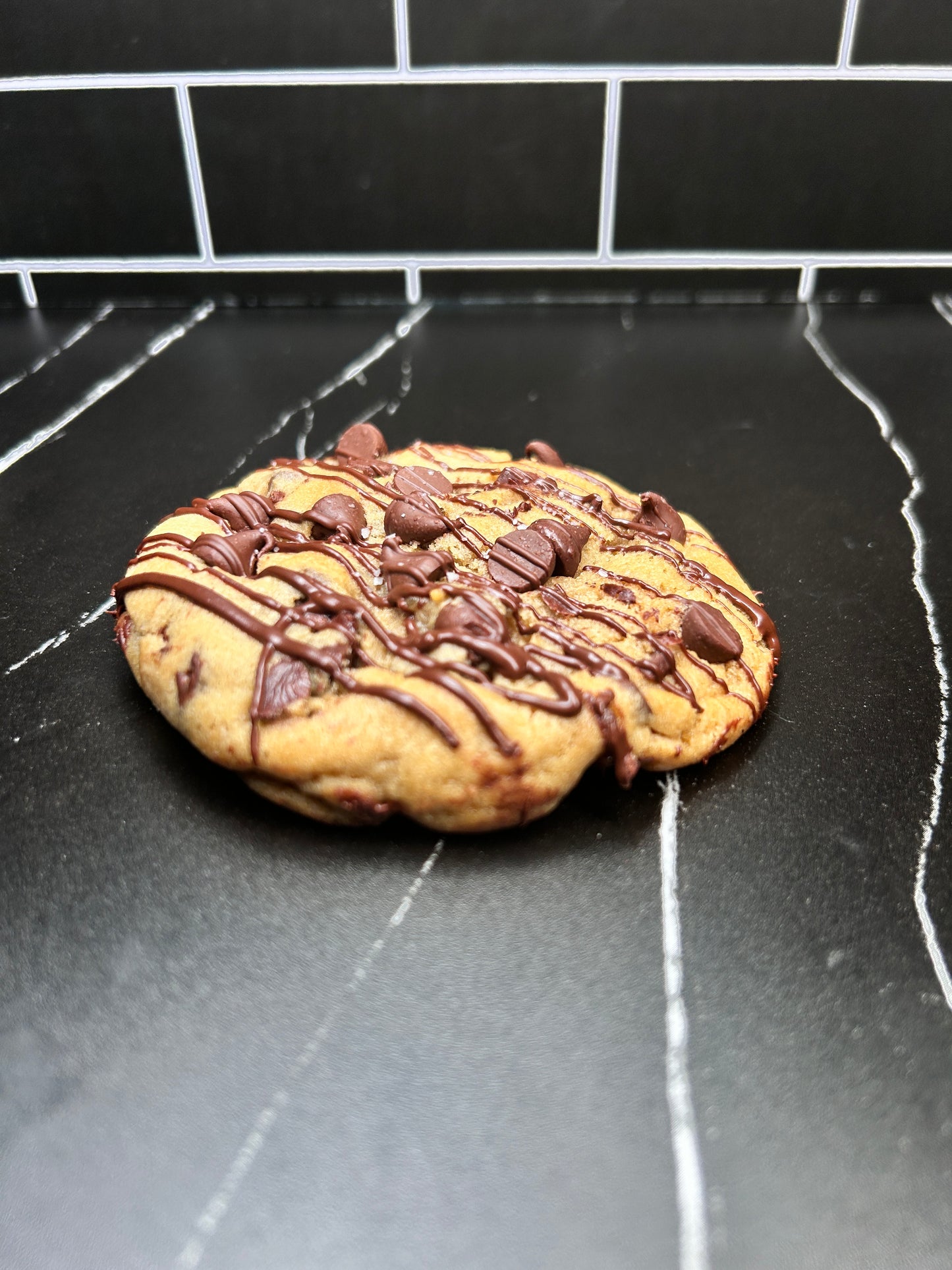 A single chocolate chip cookie with Chocolate drizzle .