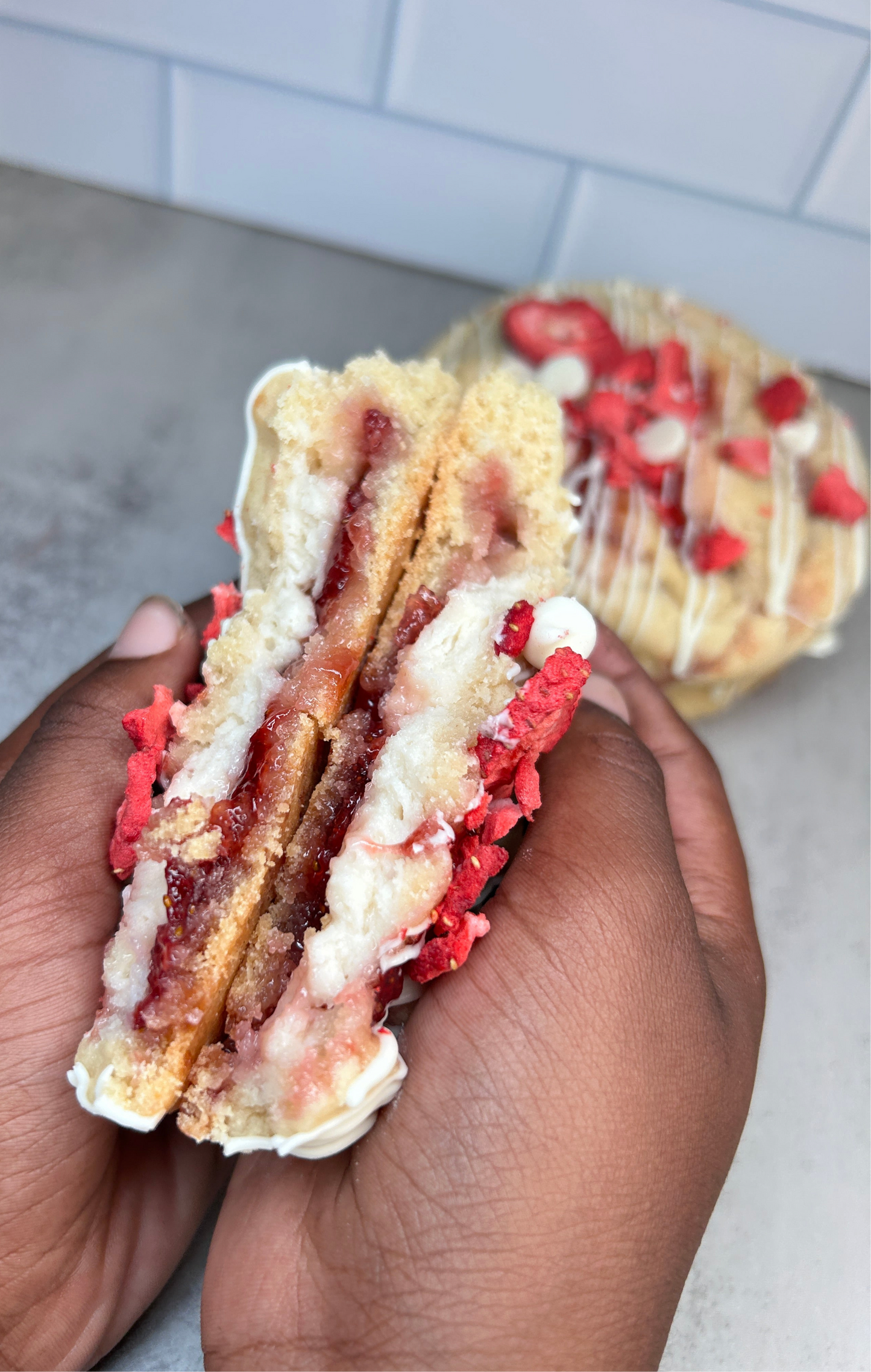 Hand holding a cookie sandwich with red and white filling, blurred background
